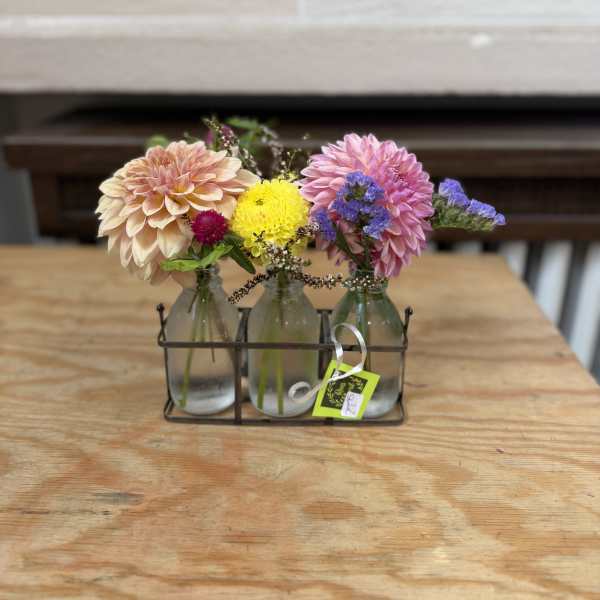 Three small glass bottles hold colorful flowers in a metal caddy.