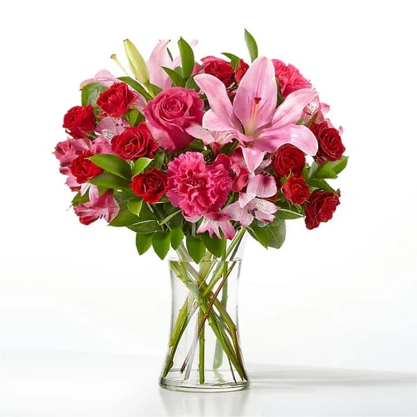 Bouquet of pink lilies, red roses, and carnations in a clear glass vase
