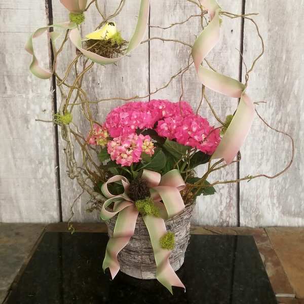 Pink hydrangea arrangement in a rustic basket with ribbon and twig accents