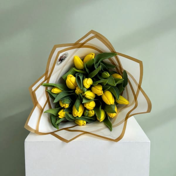Bouquet of yellow tulips wrapped in white paper with brown trim