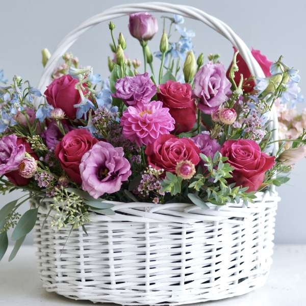 Pink and purple flowers arranged in a white wicker basket