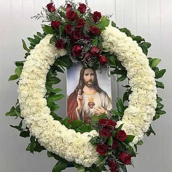 Circular funeral wreath of white flowers and red roses with a religious portrait in the center