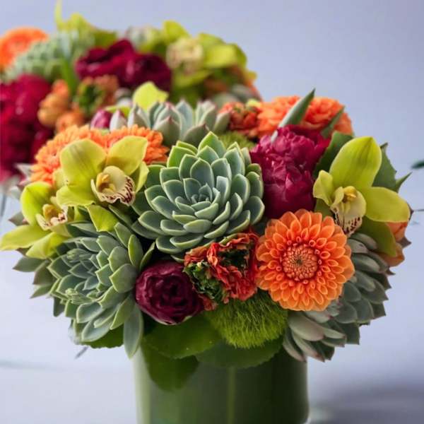 Succulent and orchid bouquet in a green glass vase