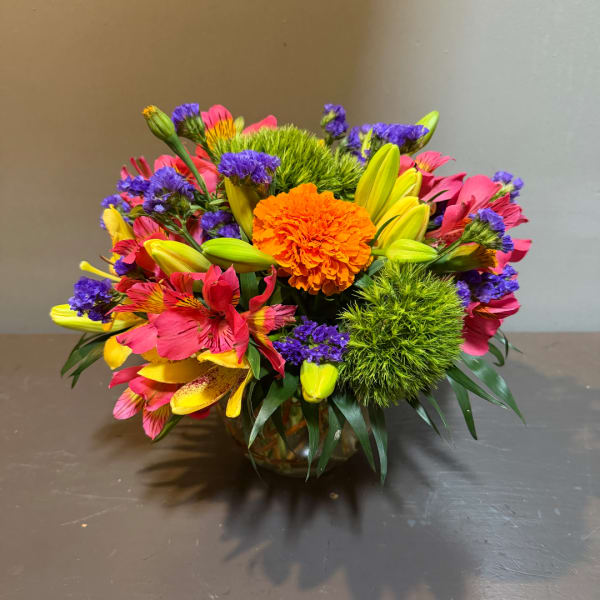 Colorful mixed bouquet in a glass vase with orange, pink, yellow, and purple blooms