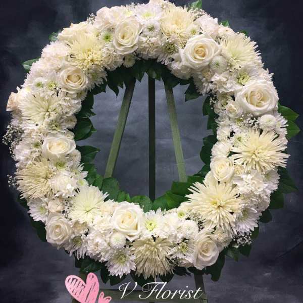 Large white rose and chrysanthemum wreath on a stand against a dark background