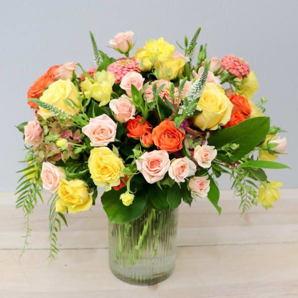 Mixed bouquet of yellow, pink, and orange roses in a glass vase