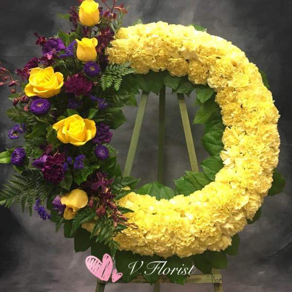 Circular floral wreath with yellow flowers and purple roses on an easel