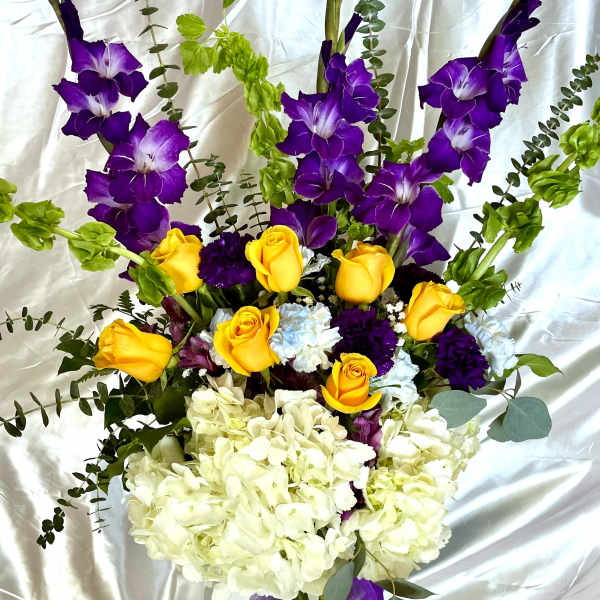 Bouquet of yellow roses, purple flowers, and white hydrangeas in a glass vase