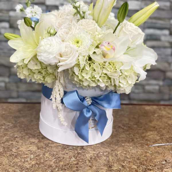 White floral arrangement in a round box with a blue ribbon
