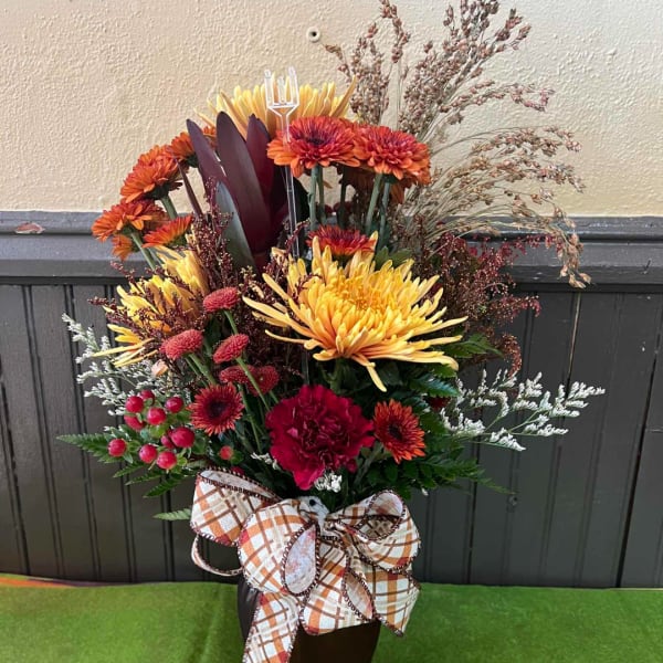 Autumn floral arrangement with yellow, orange, and red blooms in a dark vase