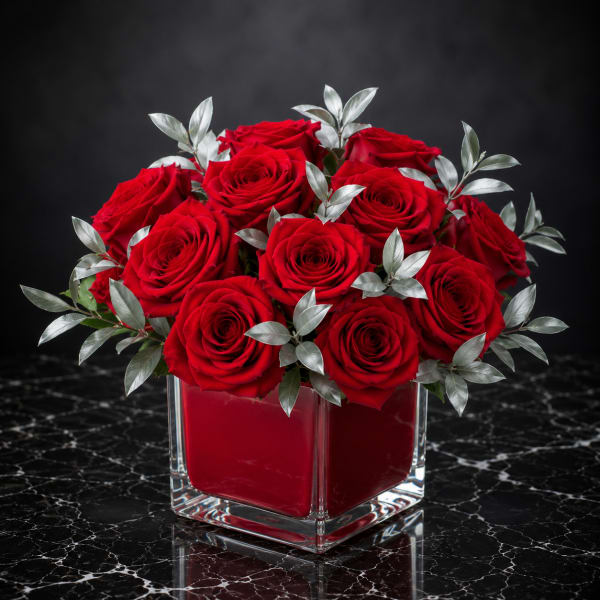 Red roses arranged in a square glass vase with silver foliage
