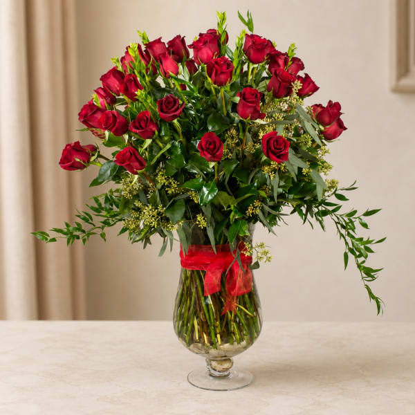 Red roses arranged in a clear glass vase with a red ribbon