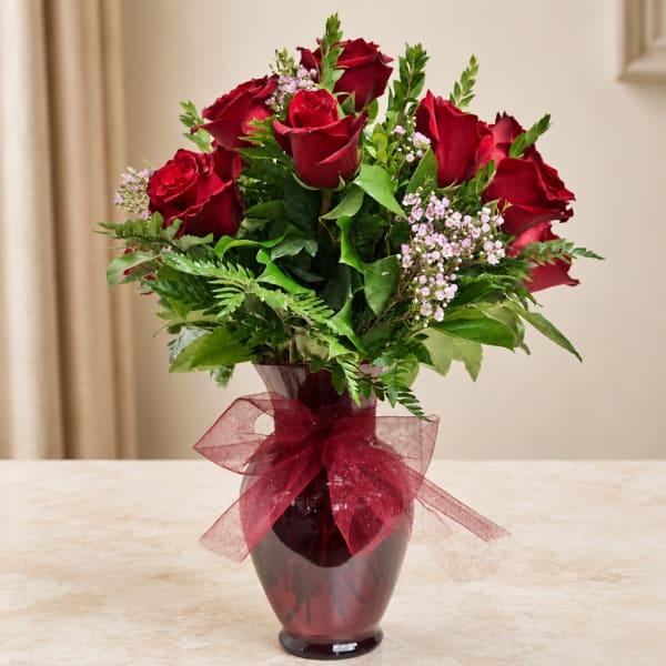 Red roses arranged in a burgundy vase with a sheer ribbon