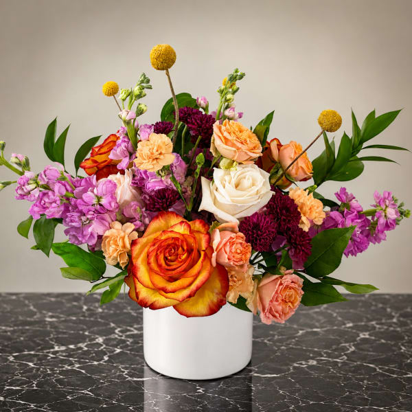Mixed bouquet of roses, carnations, and purple blooms in a white vase