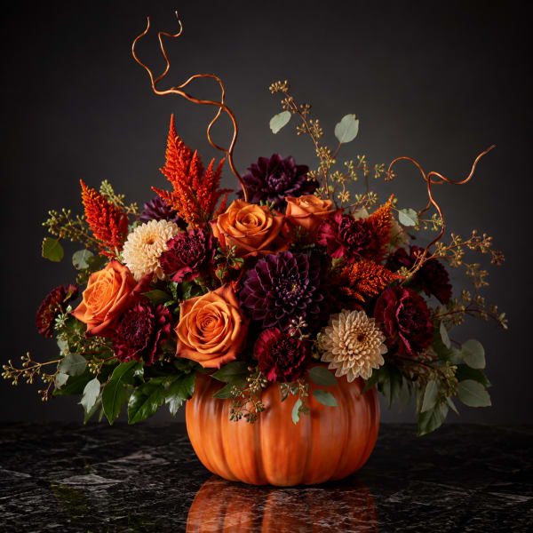 Orange and burgundy floral arrangement in a pumpkin-shaped container