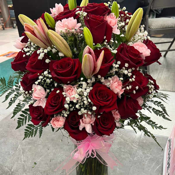 Bouquet of red roses, pink carnations, and lilies in a glass vase