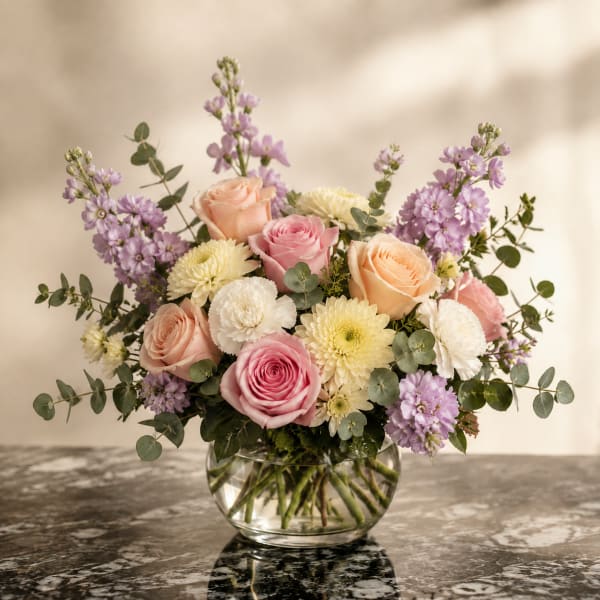 Bouquet of pink and peach roses with lavender flowers in a glass vase