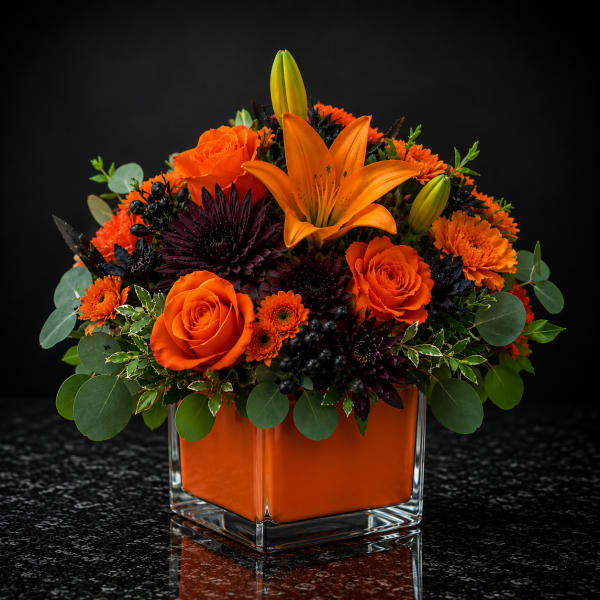 Orange roses and lilies in a square glass vase