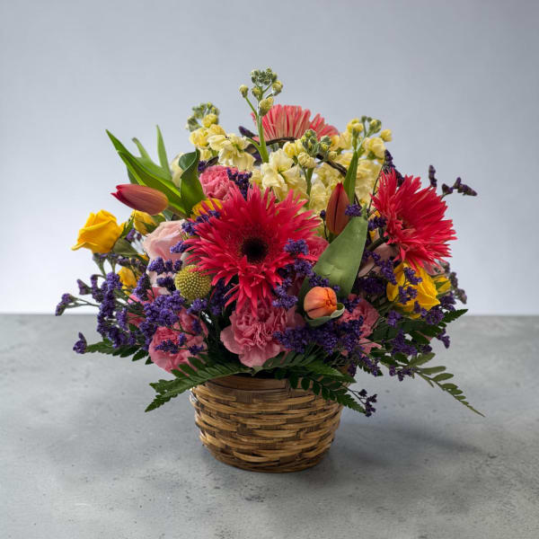 Mixed bouquet in a woven basket with pink, yellow, and red flowers