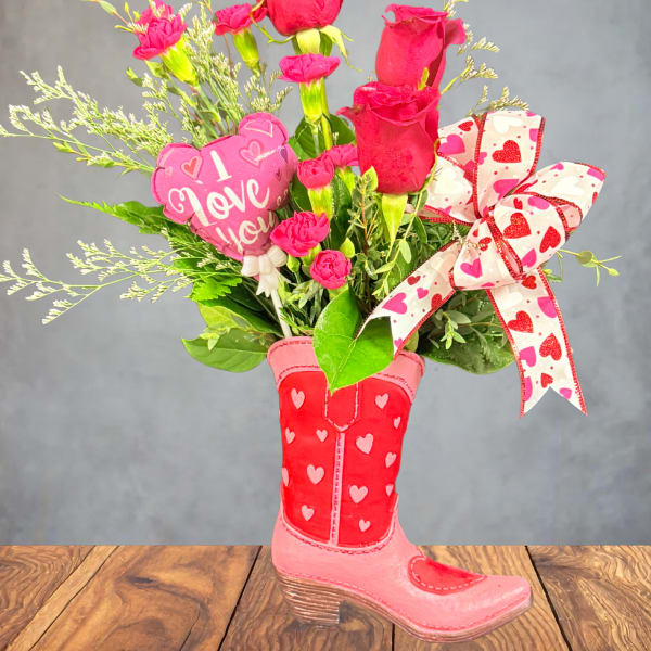 Pink roses and carnations arranged in a heart-decorated boot vase with a ribbon.