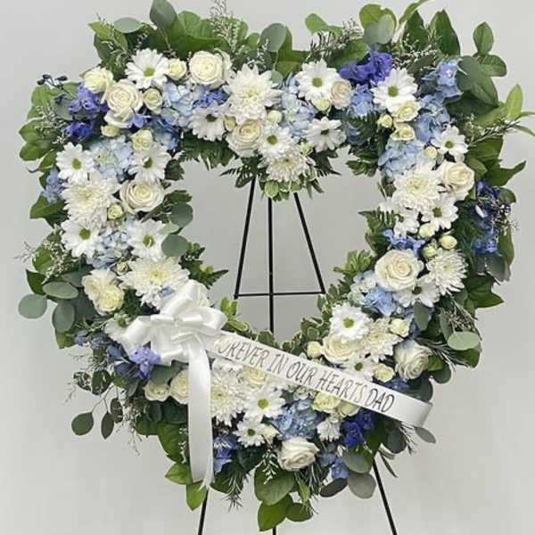 Heart-shaped floral wreath on a stand with a white ribbon