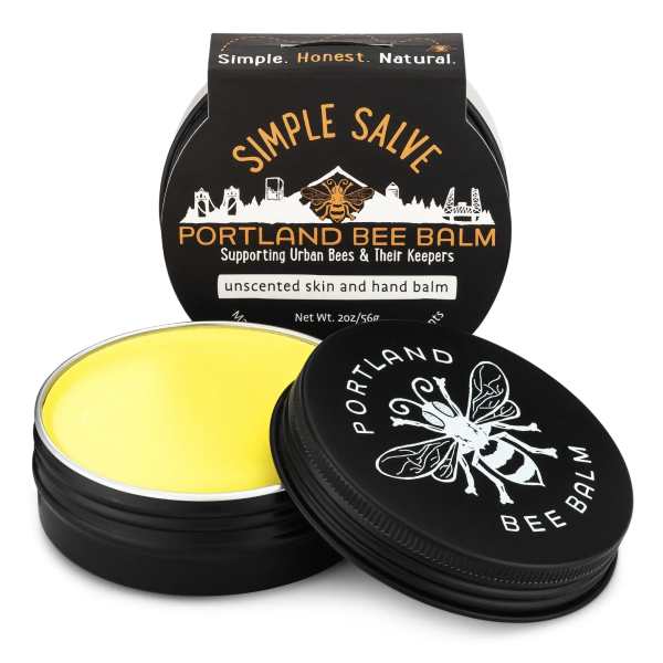 Two black tins of Portland Bee Balm with one open showing yellow balm