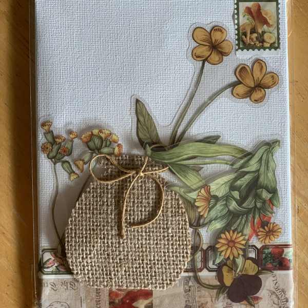 Decorative card with pressed flowers and a burlap pouch on a textured white background
