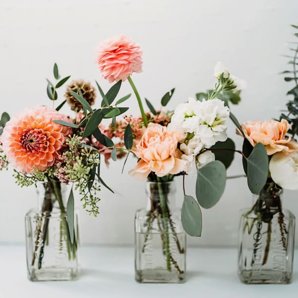 Three small floral arrangements in glass bottles with peach and white blooms