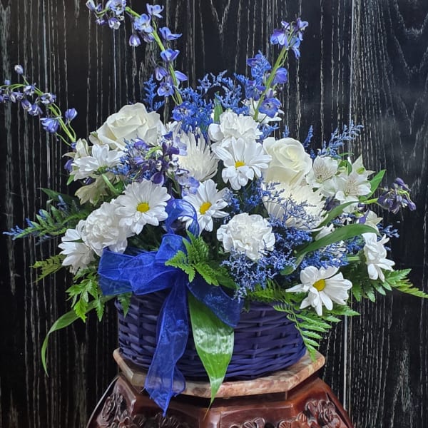 Blue and white flower arrangement in a woven basket with a ribbon