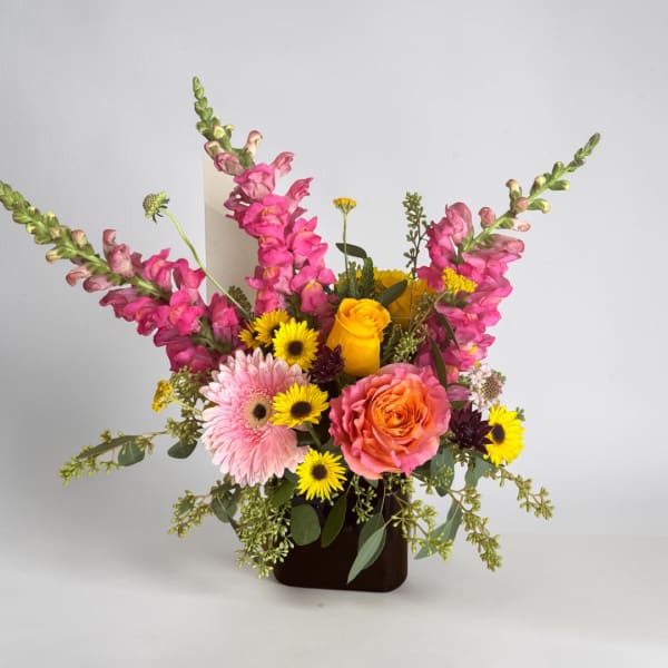 Mixed bouquet with pink snapdragons, roses, gerbera daisies, and yellow daisies in a dark vase