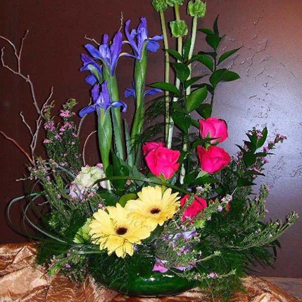 Mixed bouquet with pink roses, yellow gerberas, and purple irises in a green vase