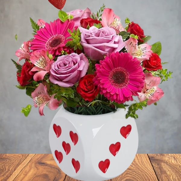 Pink and red flower arrangement in a white heart-decorated vase with a red heart pick