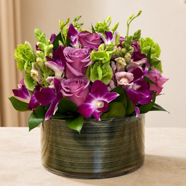 Purple roses and orchids arranged in a glass vase