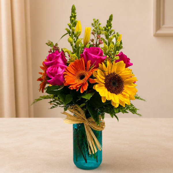 Bright mixed bouquet with roses, gerbera daisies, and sunflowers in a blue vase