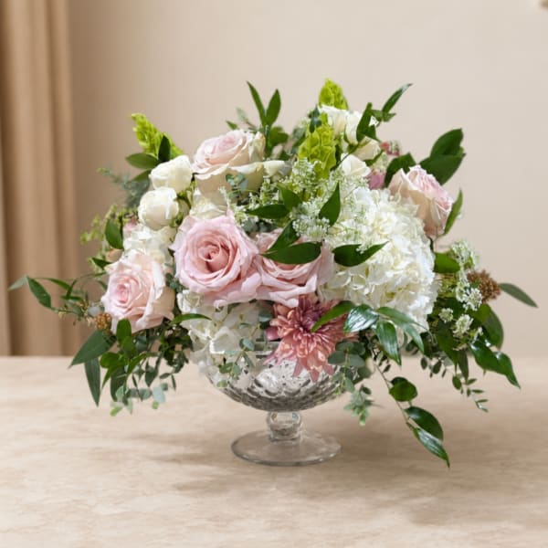 Pink and white roses with hydrangeas in a clear pedestal vase