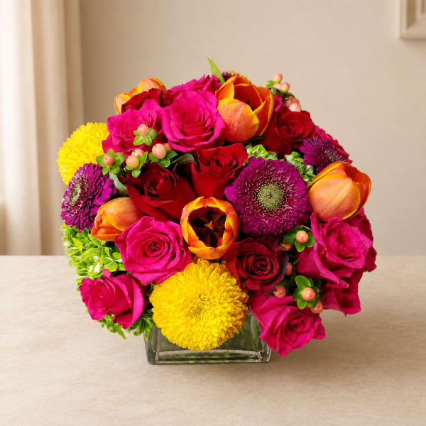 Bright mixed bouquet in a square glass vase with roses and tulips