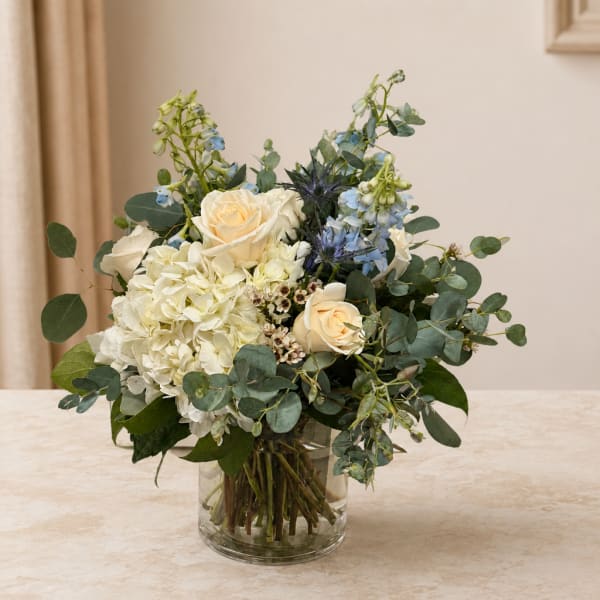 White roses and hydrangea in a clear glass vase with blue flowers