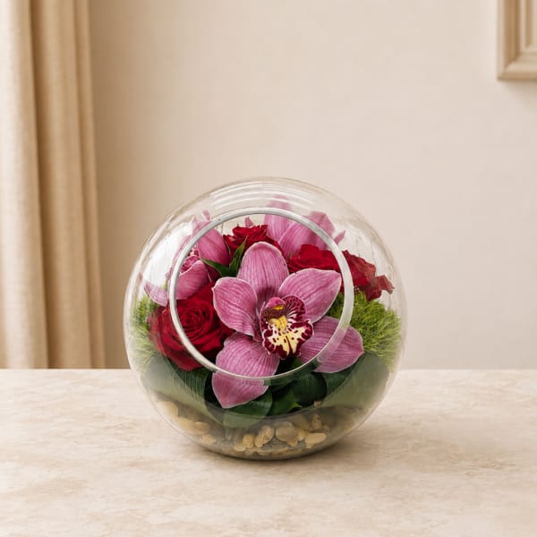 Pink orchids and red roses in a clear round glass vase
