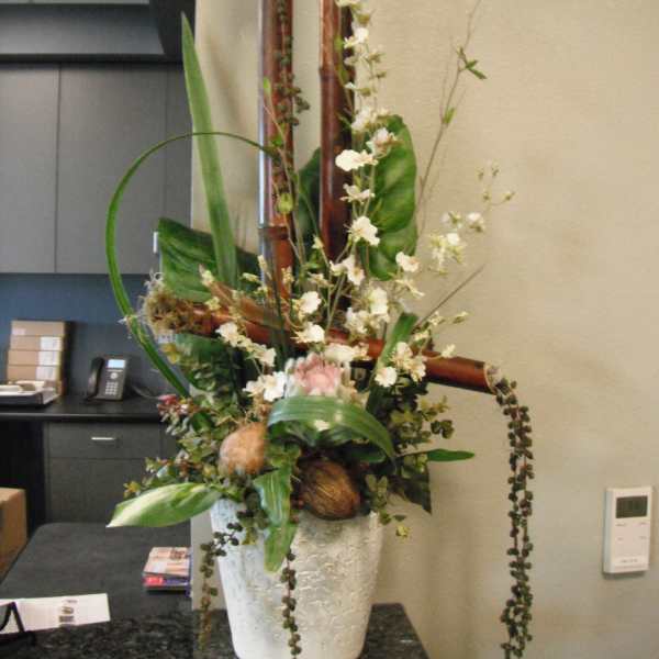 Tall floral arrangement in a white textured pot with white blossoms and greenery