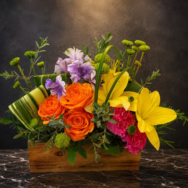 Bright mixed flower arrangement in a wooden box with orange roses and yellow lilies