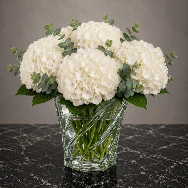 White hydrangea bouquet in a clear glass vase with eucalyptus accents