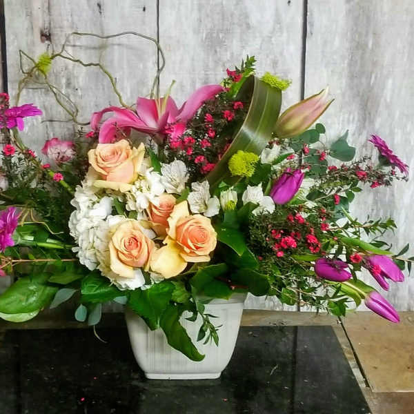Mixed floral arrangement in a white square vase with pink lilies and roses