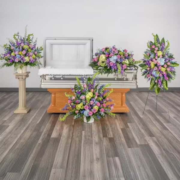 Set of pastel funeral flower arrangements surrounding an open casket in a chapel.