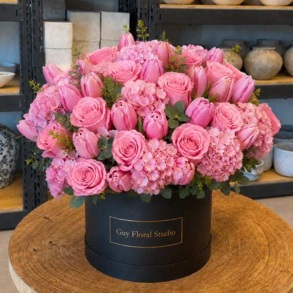 Pink roses and tulips arranged in a black round box