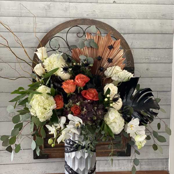 Mixed floral arrangement in a silver vase with white, orange, and dark blooms