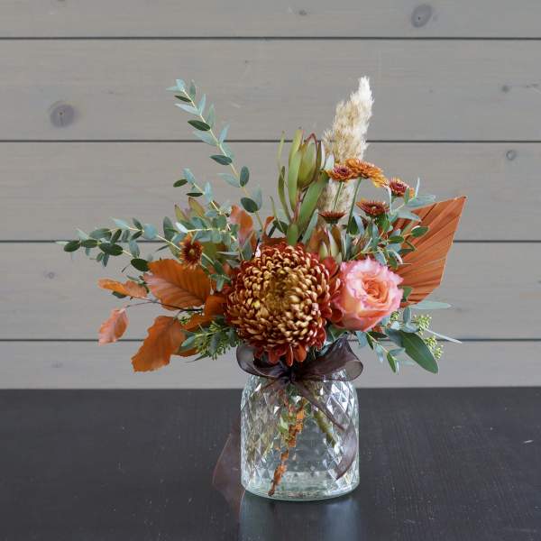 Orange and pink floral arrangement in a glass vase with a ribbon