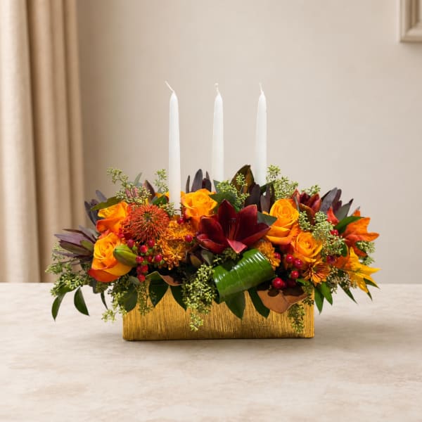 Orange and red floral centerpiece with three white candles in a gold container