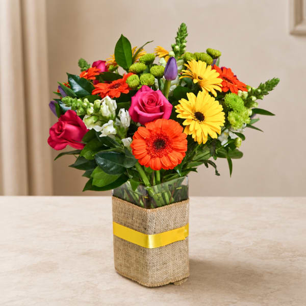 Mixed bouquet of roses, gerbera daisies, and snapdragons in a wrapped glass vase