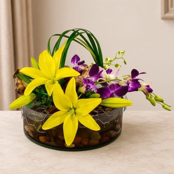 Yellow lilies and purple orchids arranged in a glass bowl