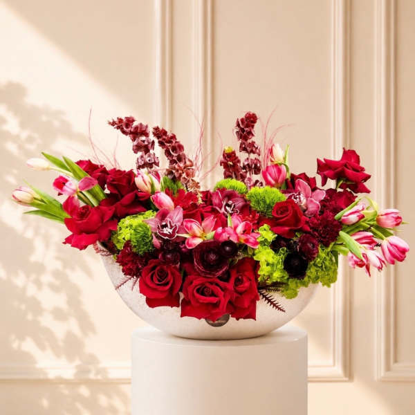 Large red and pink floral arrangement in a white bowl vase